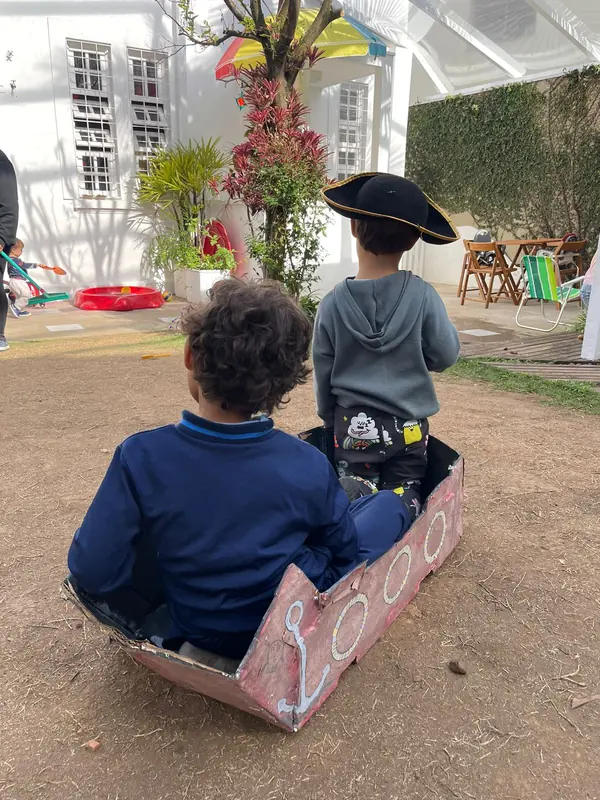 Duas crianças brincando dentro de um barco de papelão no quintal.
