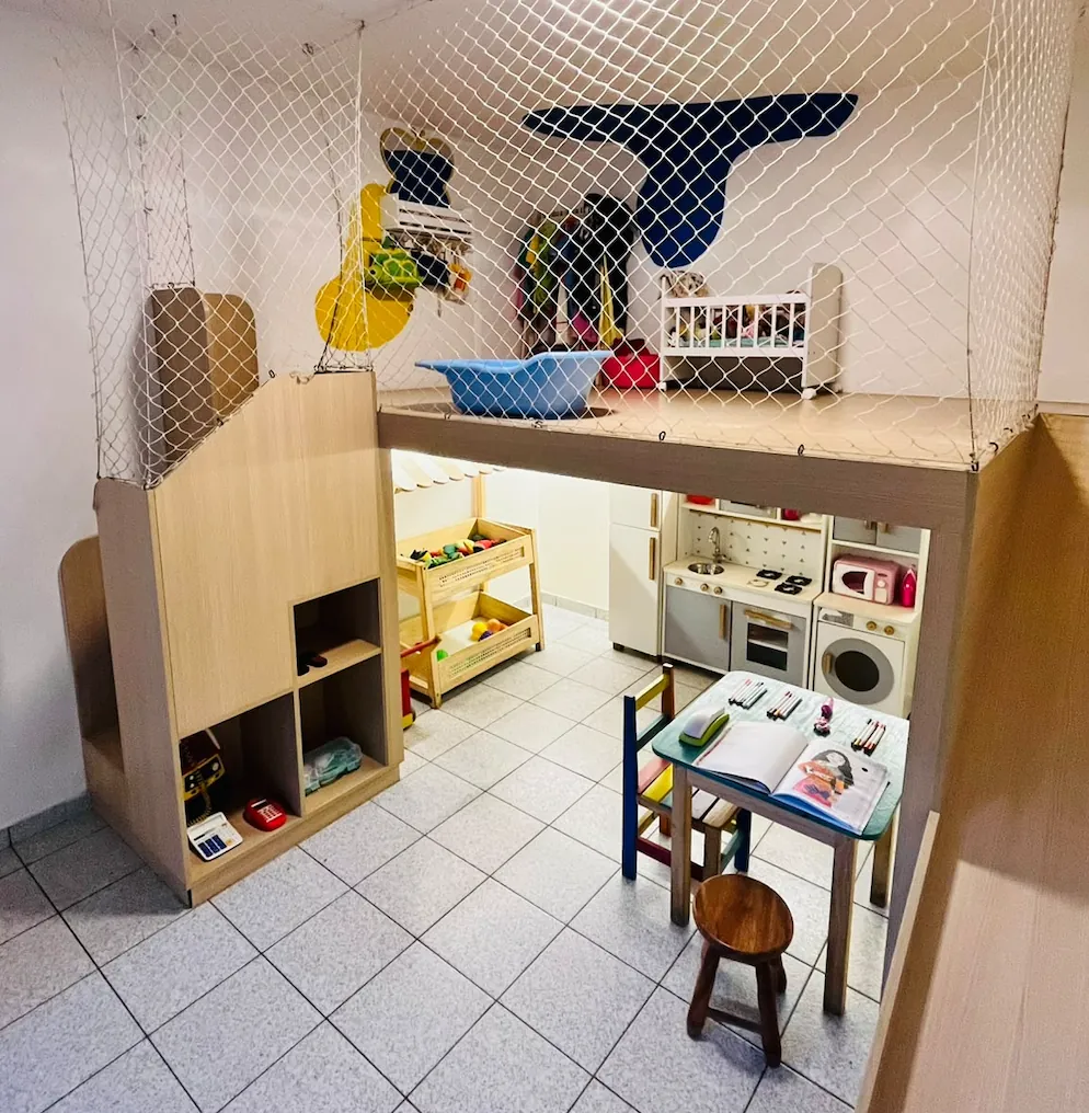 Casinha de madeira com mezanino e rede de proteção, cozinha de faz de conta e mesinha de leitura embaixo.