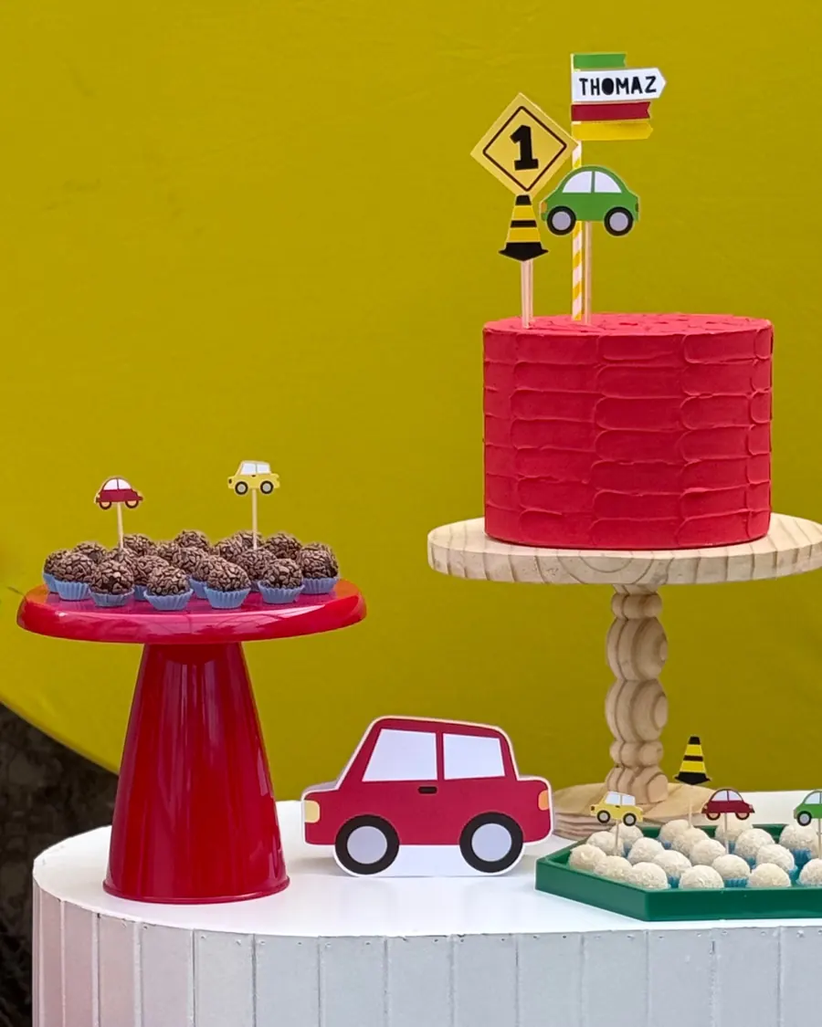 Mesa com tema de carrinhos: bolo vermelho com topo de sinalização, brigadeiros e painel amarelo.