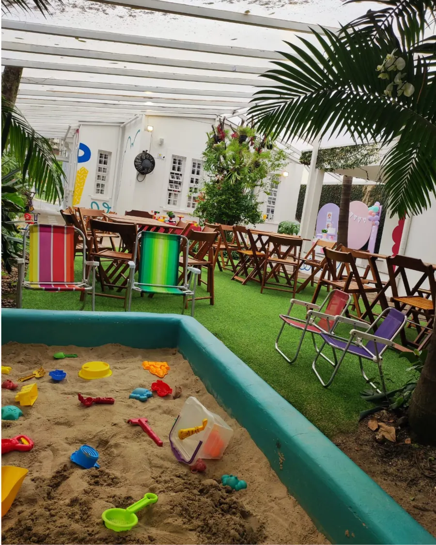 Quintal preparado para a festa: mesas e cadeiras montadas ao redor do tanque de areia, com a decoração ao fundo.