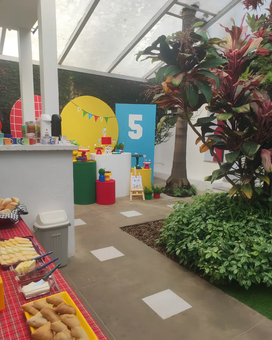 Mesa do bolo decorada em azul, amarelo e vermelho, ao lado da mesa de comidas montada.