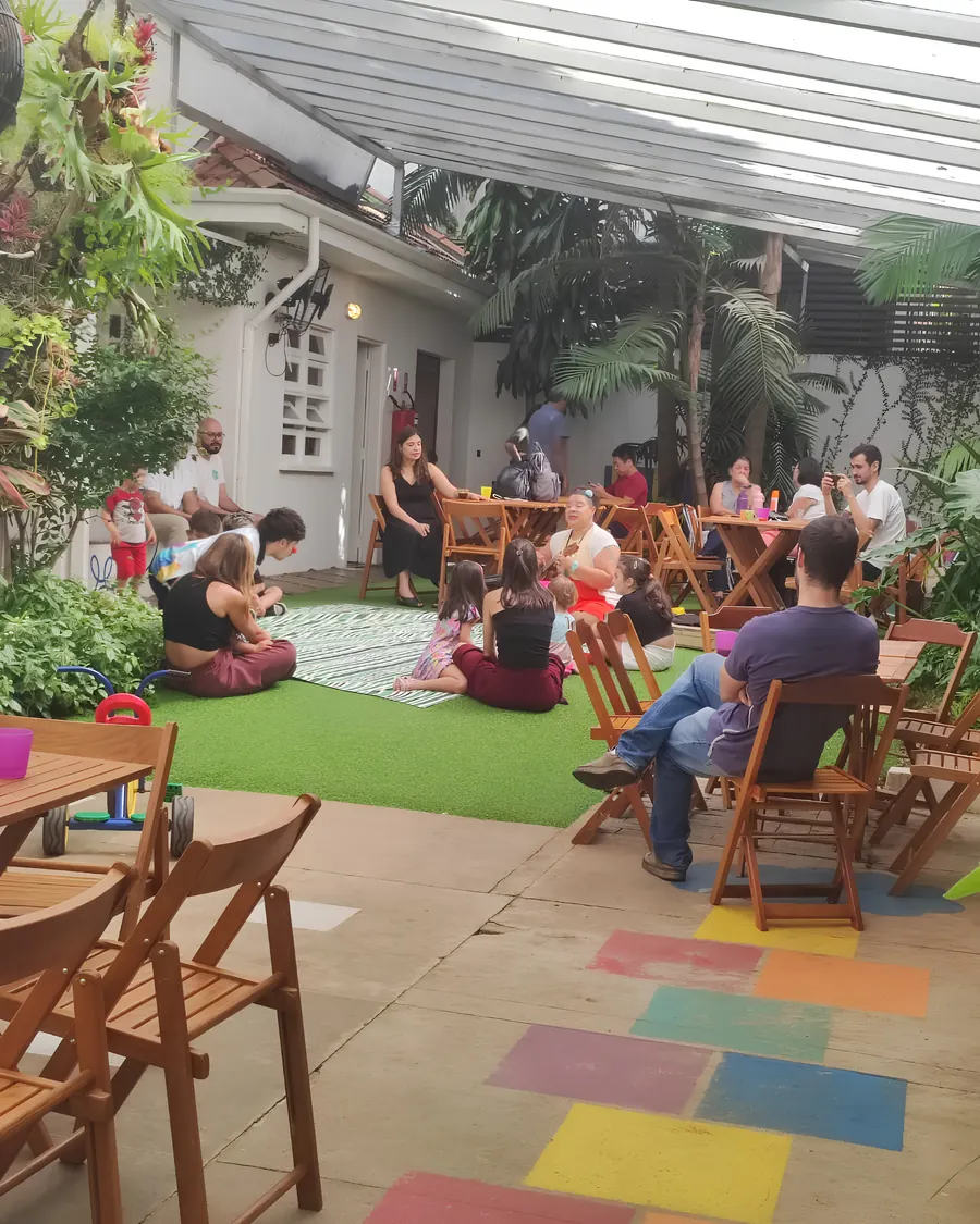 Famílias sentadas nas mesas e crianças na grama durante uma roda de música na festa.