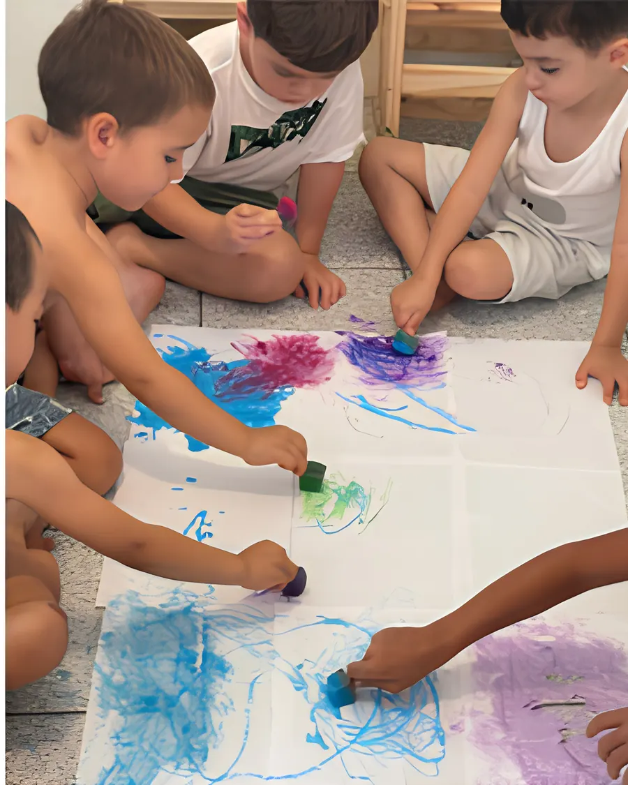 Crianças carimbando tinta azul, rosa e roxa em folhas grandes de papel no chão.