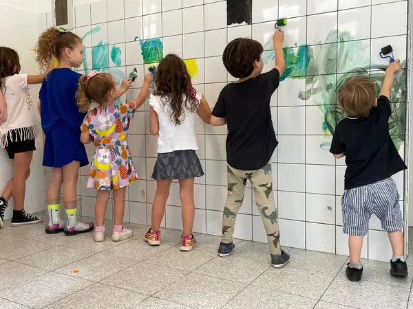 Crianças pintando o muro de azulejo com rolinhos de tinta.