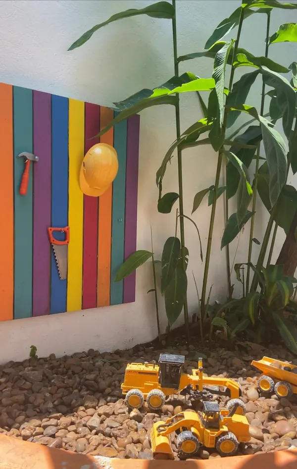 Tanque de pedras com máquinas de brinquedo, painel colorido de madeira e ferramentas na parede.